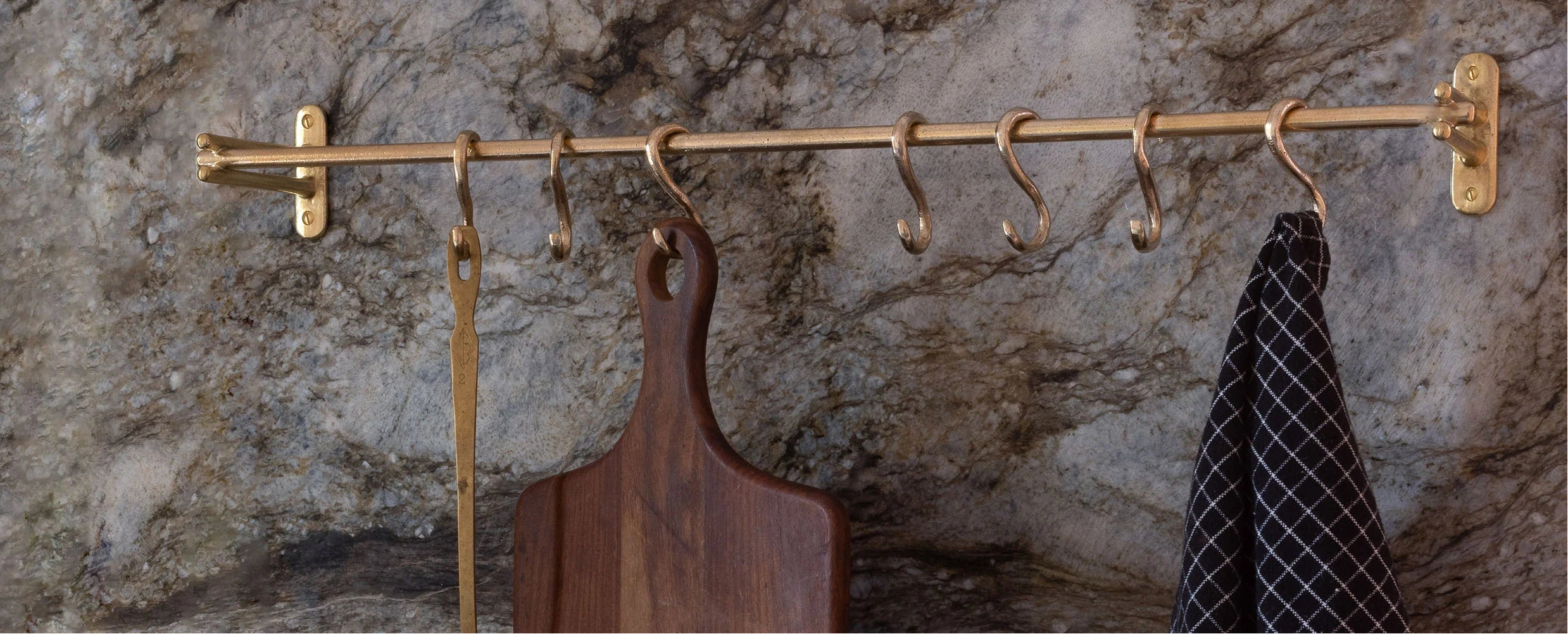 Brass wall-mounted hook rack with various items on a stone wall background