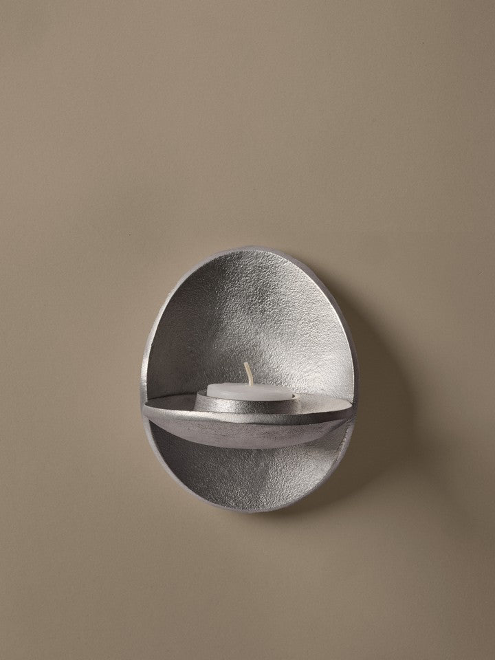Silver wall-mounted candle holder with a candle on a beige background
