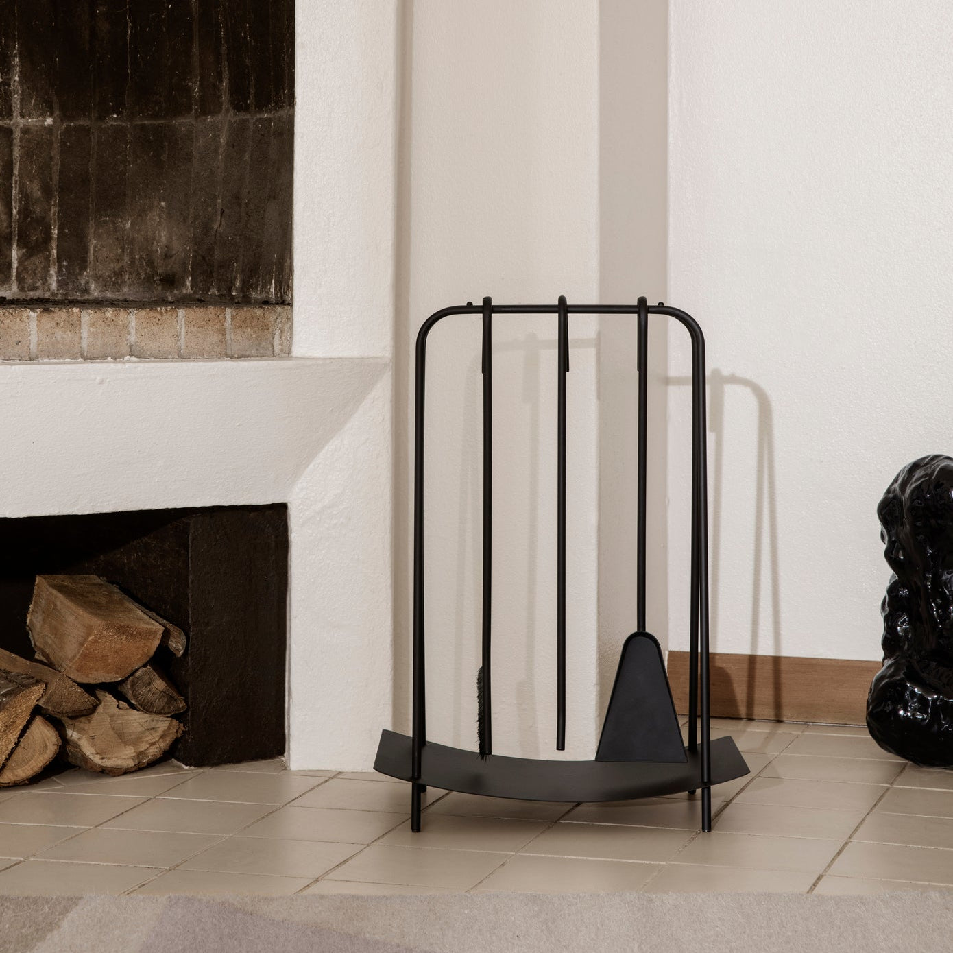 Black metal firewood holder in front of a fireplace with logs inside